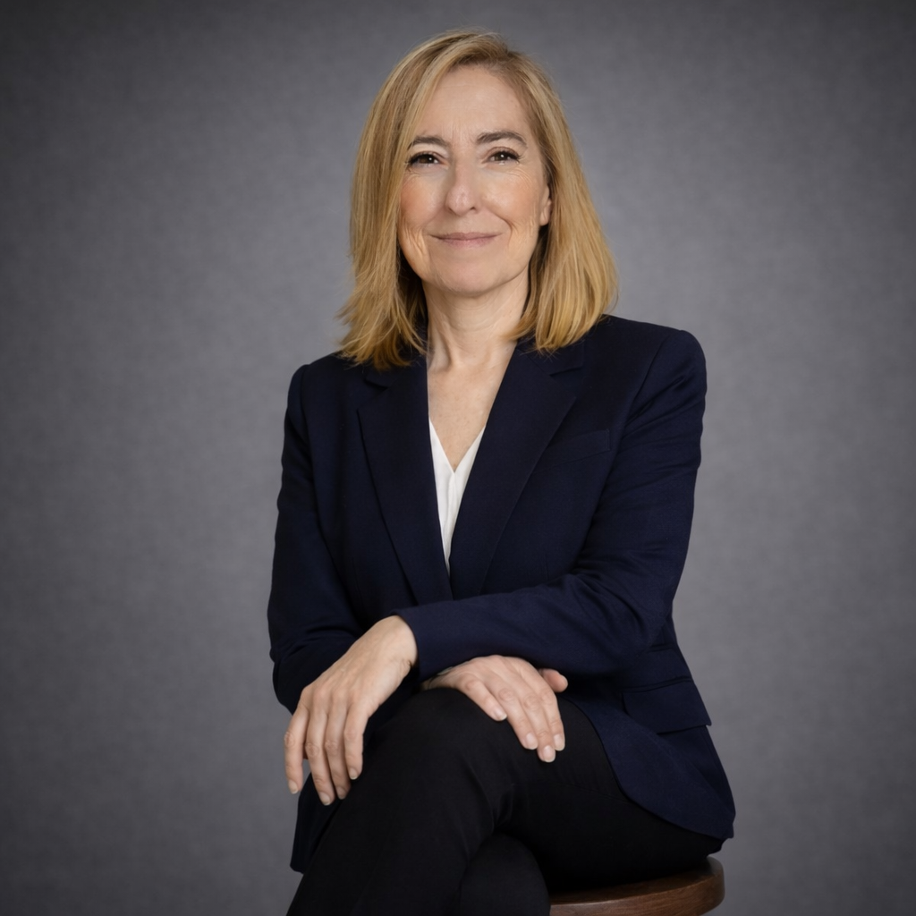 Retrato profesional de Marta, coach personal para personas en etapa de prejubilación y seniors, con expresión cercana y confiable, vestida con blazer azul oscuro, fondo minimalista gris y aspecto natural